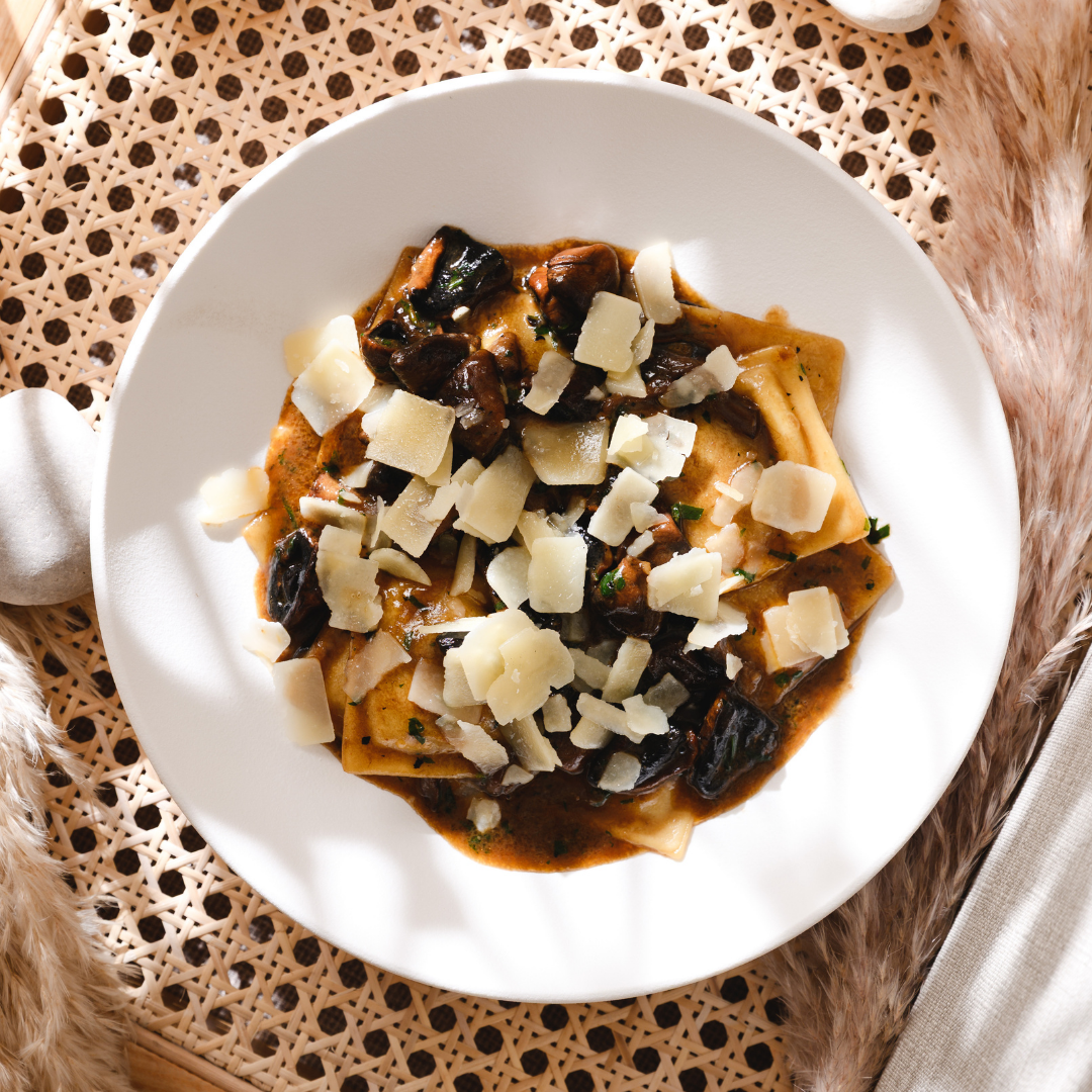 Pasta with mushrooms and shaved parmesan on a white plate at a woven table setting